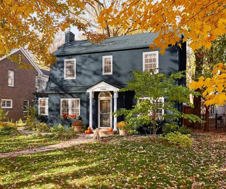 a blue house in the fall with yellow leaves on the ground and trees around it