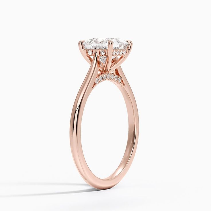 a rose gold engagement ring with three stones on the band and an oval shaped center stone