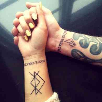 two people holding hands with tattoos on their wrists and wristbands, both showing symbols