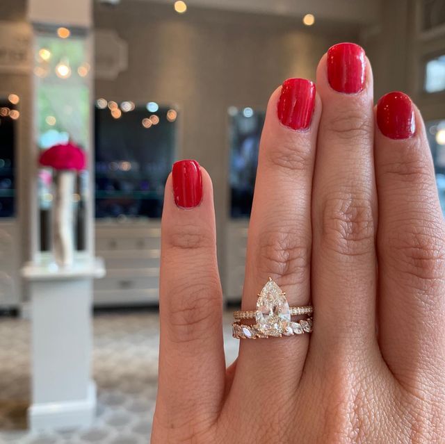 a close up of a person's hand with a red manicure holding a diamond ring