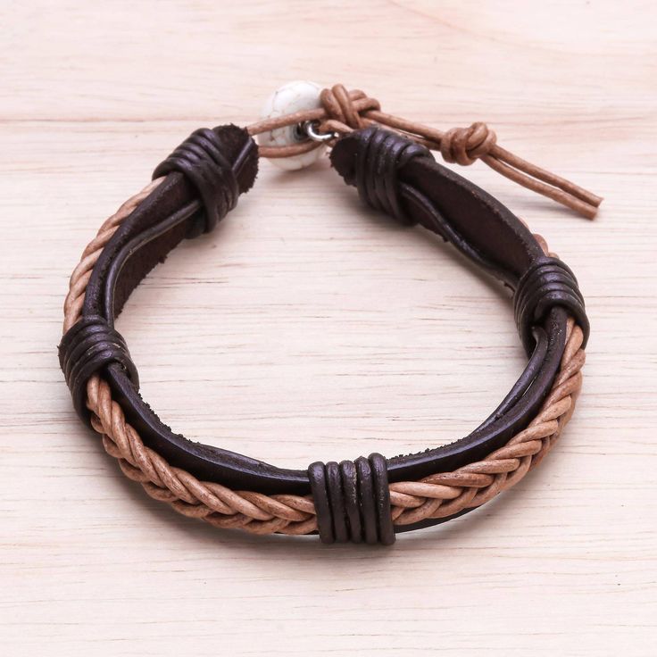 Circling the wrist hand-braided leather cord in black decorates a dark brown wristband. Thailand's Chaloemphon presents this bracelet crafted by local artisans. An adjustable howlite button clasp completes this accessory. Adjustable Brown Leather Braided Bracelet, Brown Braided Leather Bracelet In Bohemian Style, Adjustable Brown Braided Jewelry, Adjustable Braided Brown Jewelry, Adjustable Brown Leather Bracelet With Black Band, Brown Leather Braided Jewelry, Black Leather Bohemian Braided Bracelets, Bohemian Black Leather Braided Bracelets, Brown Braided Leather Jewelry