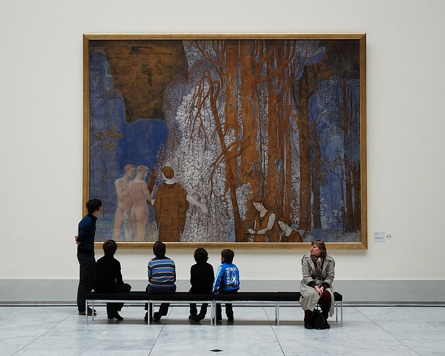 four people sitting on a bench in front of a painting