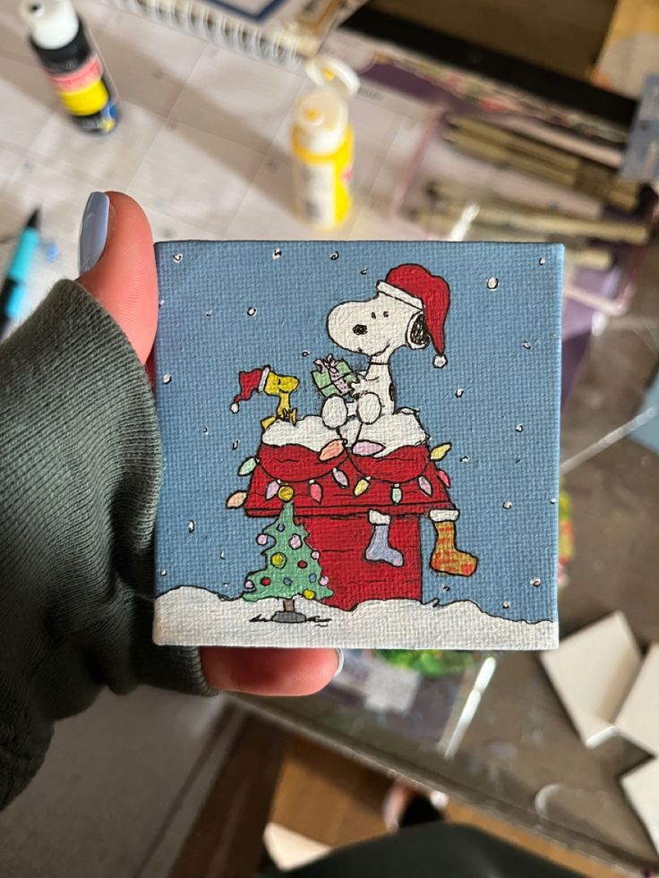 a hand holding up a small card with a snoopy christmas scene on the front