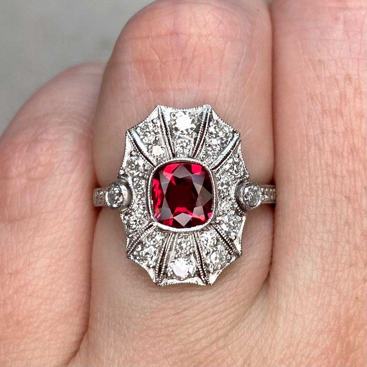 This platinum ring features a bezel-set 0.97-carat cushion cut natural Burma ruby, surrounded by pave-set diamonds. Two bezel-set accent diamonds and pave-set shoulders draw the eye towards the center stone. The ring also displays fine milgrain and geometric cutouts in the under-gallery. This ring is an antique recreation inspired by the Art Deco era.
The measurements of the ruby are approximately 6.24mm x 5.75mm x 2.60mm.
This ring can be resized to any finger size at no extra cost.
Ready to Ma Art Deco Diamond Jewelry With Gemstone, Luxury Silver Ruby Ring With Single Cut Diamonds, Cushion Cut Diamond Ring With Accent Stones In Platinum, Cushion Cut Platinum Diamond Ring With Accent Stones, Platinum Cushion Cut Diamond Ring With Accent Stones, Art Deco Ruby Ring With Diamond Details, Ruby Ring With Diamond Accents Fine Jewelry, Dazzling Ruby Diamond Ring, Luxury Ruby Jewelry Radiant Cut