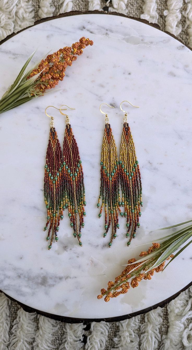 two pairs of beaded earrings sitting on top of a white marble table next to dried flowers