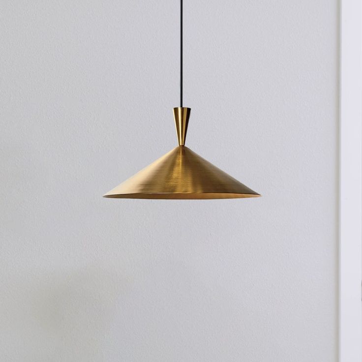 a gold colored pendant light hanging from a white wall next to a black table and chair