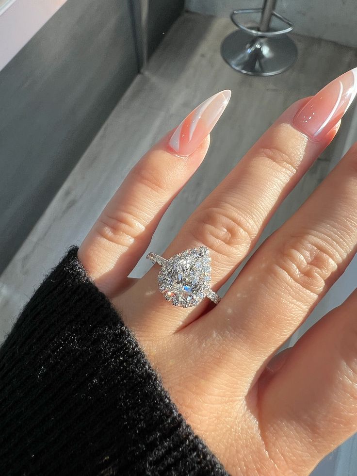 a woman's hand with pink and white manicured nails holding a diamond ring