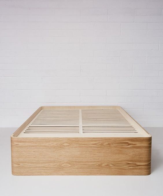 a wooden bed frame sitting on top of a white floor next to a brick wall