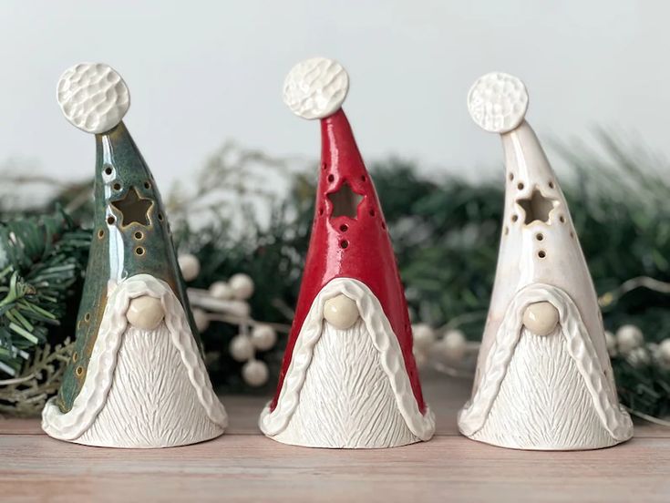 three small christmas hats sitting on top of a table next to pine cones and greenery