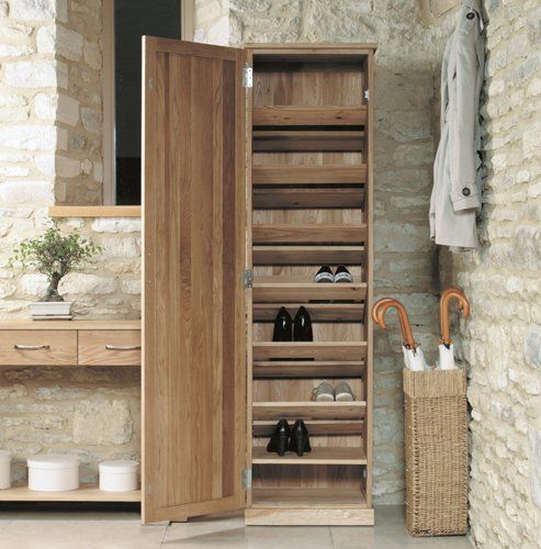 an open wooden cabinet with shoes and umbrellas in it next to a stone wall