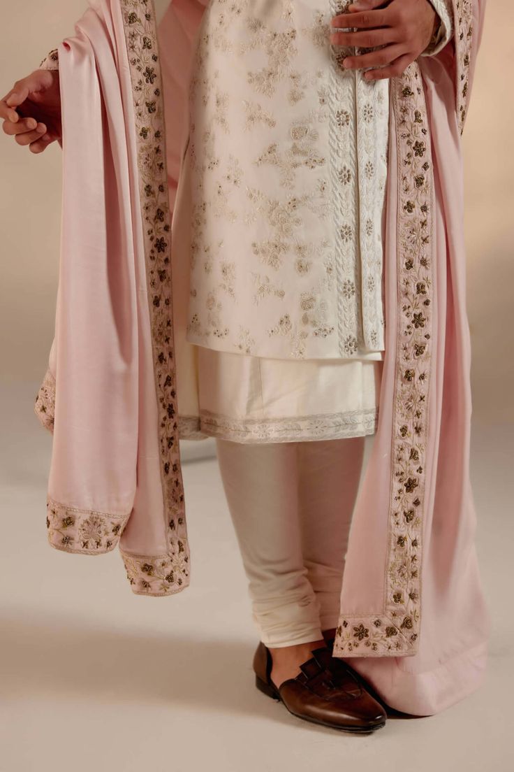 Editor's Note Featuring our work of art in our white all-over hand-embroidered sherwani set. The foundation is crafted using tone-on-tone thread along with silver zari work as a base texture. Paired with a baby pink hand-embroidered stole safa. Fabric: Linen silk Color: White Components: Sherwani, kurta, churidar, stole, safa and cummerbund Occasion: Groom Fit: Regular Note: Product colour may slightly vary due to photographic lighting sources Care: Dry clean only About the Designer After establ Pink Bandhgala With Dabka Work, Festive Elegant Sherwani With Sheer Dupatta, Festive Pink Sherwani With Dabka Work, Pink Bandhgala With Dabka Work In Traditional Drape, Elegant Semi-stitched Sherwani With Sheer Dupatta, Transitional Silk Sherwani With Chikankari Embroidery, Elegant Sherwani With Sheer Dupatta For Eid, Pink Sherwani With Resham Embroidery In Traditional Drape, White Silk Sherwani With Resham Embroidery