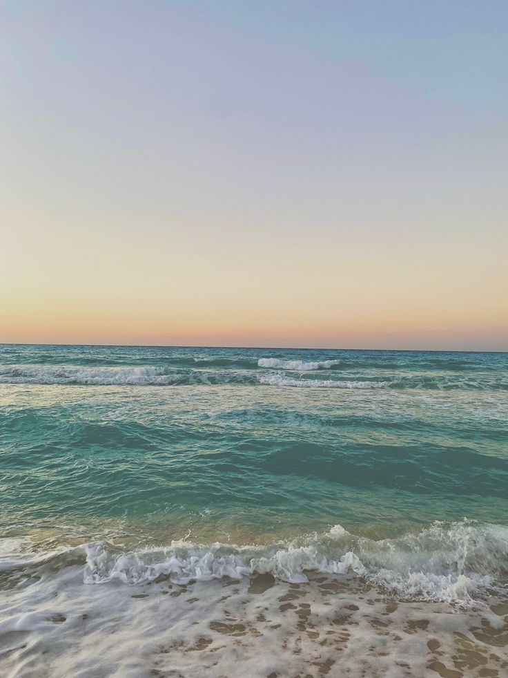 the ocean with waves coming in to shore and a blue sky above it at sunset