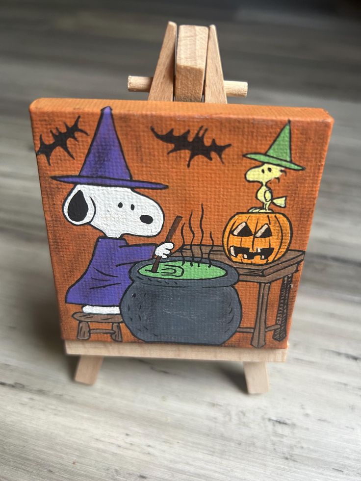 a small wooden easel with a snoopy halloween painting on it's side