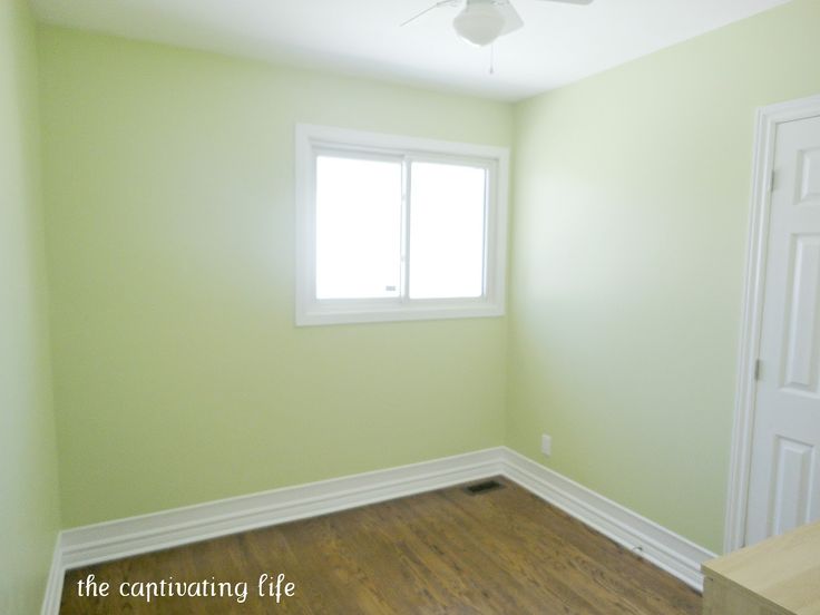 an empty room with hard wood floors and green walls, white trim on the windows