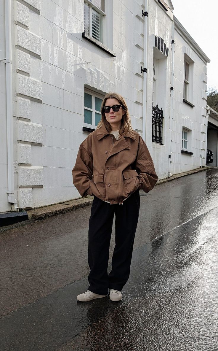 A woman stands in front of a white house. She wears black sunglasses, a short brown jacket, black trousers and white canvas shoes. Short Coat Outfit, Short Jacket Outfit, Casual Weekend Outfit, Studio Nicholson, Casual Outfit Inspiration, Spring Jacket, Jacket Outfit, Casual Weekend, Spring Jackets