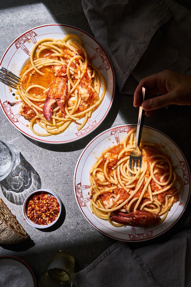 two plates of spaghetti with lobsters and tomato sauce on them, one being eaten by a fork