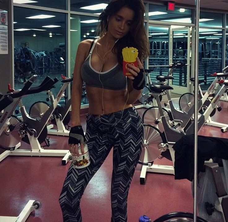 a woman standing in a gym holding a drink