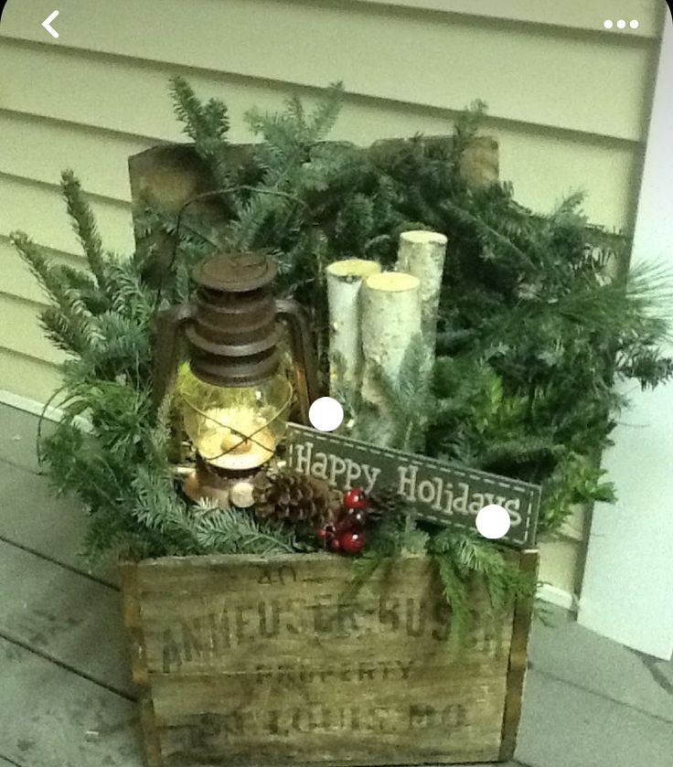 a wooden crate filled with pine cones and candles on top of a porch next to a christmas tree