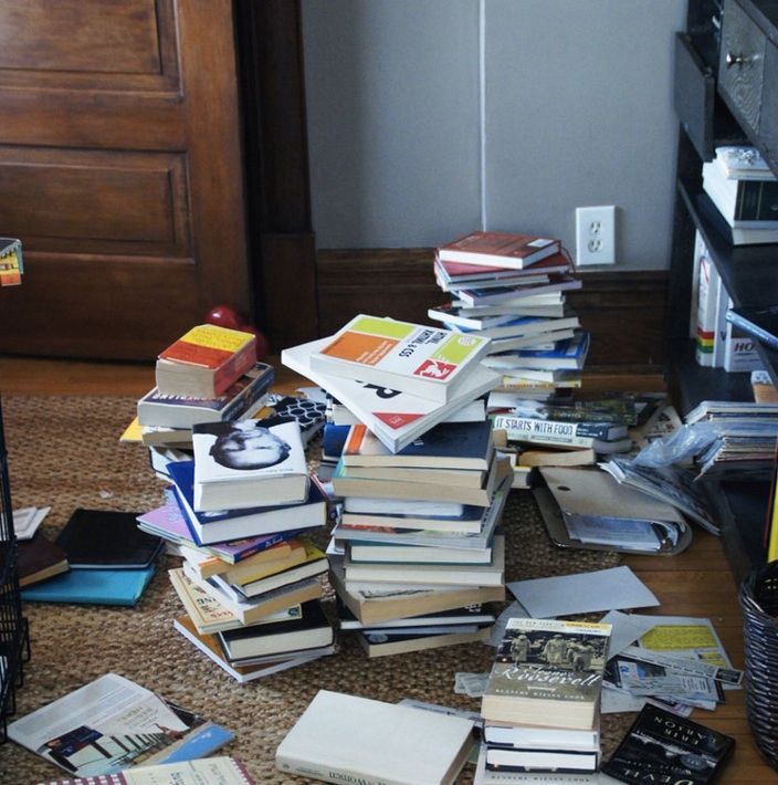 a pile of books sitting on top of a floor next to a book shelf filled with books