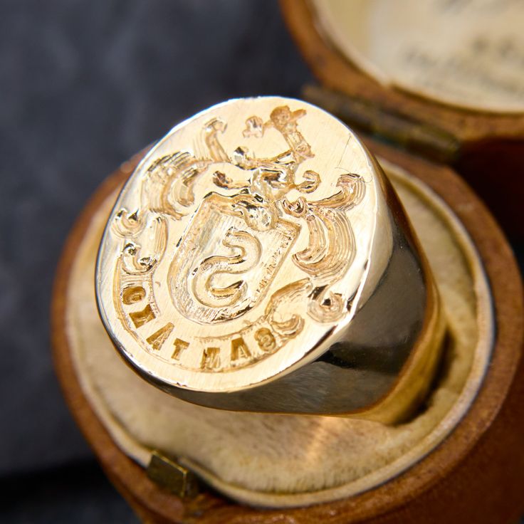 a gold ring with an emblem on it sitting in a wooden box next to another one