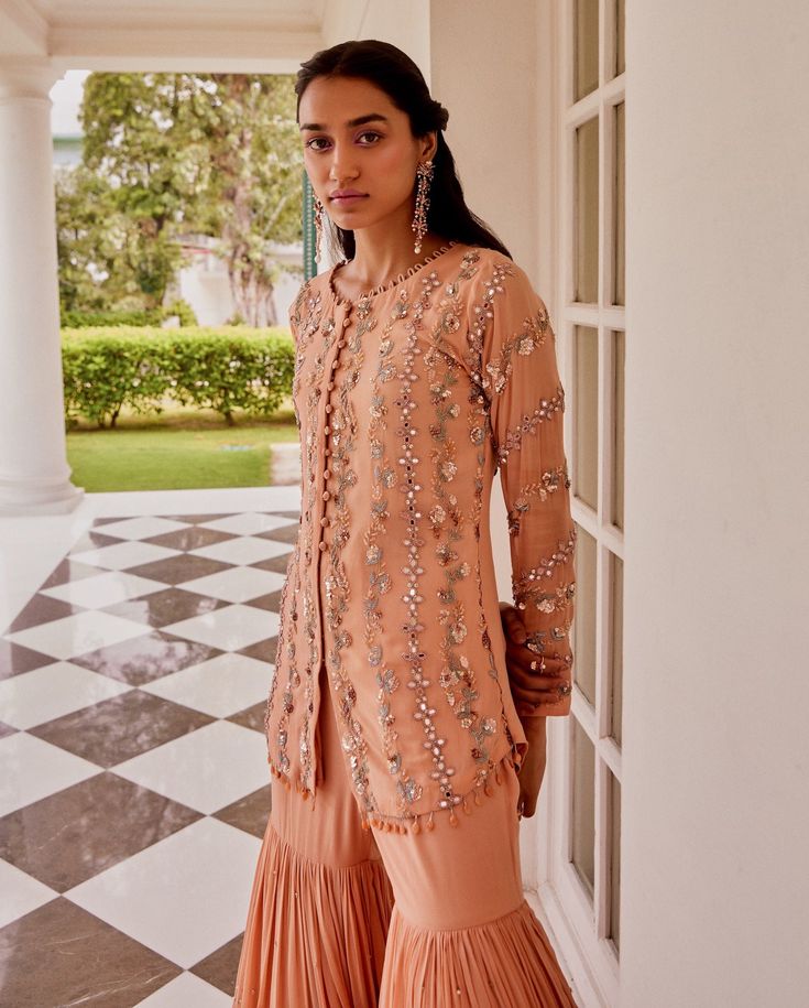 Editor's Note This set features Full sleeves kurta with overall hand embroidery in alternate mirror work and floral stripes. It has faux potli button detailing. It is paired with a tiered cheeta embroidered sharara Color: Rose Gold Fabric: Georgette and net Care: Dry Clean Only About the Designer Sanya gulati's designs are inspired by the Indian bridesmaids, pastel easy hues & the seasonal trends, her designs is a mix of modern, contemporary embroideries with traditional silhouettes thus creatin Embellished Sharara With Straight Kurta For Eid, Navratri Embellished Palazzo Set With Straight Kurta, Bollywood Style Embellished Sharara With Straight Kurta, Eid Long Sleeve Palazzo Set With Gota Work, Navratri Long Sleeve Embellished Kurta, Embellished Sharara For Eid, Long Sleeve Embellished Kurta For Navratri, Designer Wear Embellished Sharara With Straight Kurta, Embellished Long Sleeve Kurta For Navratri