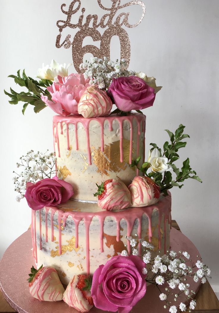 a three tiered cake with pink and white frosting, roses, and greenery