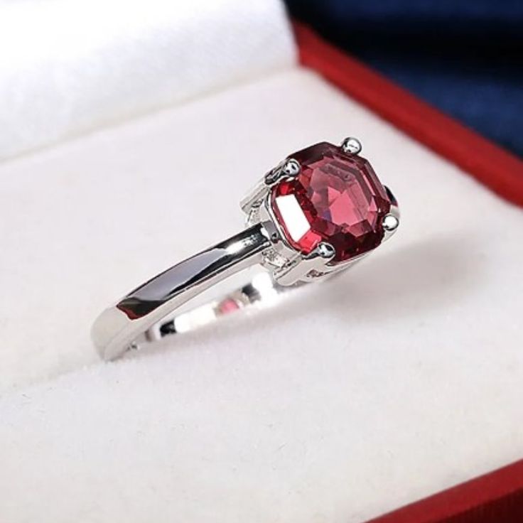 a close up of a ring in a box with a red stone on it's side