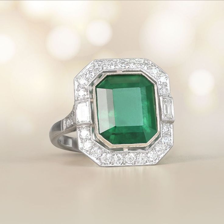 This ring features a 4.97-carat emerald-cut natural emerald bezel-set in 18k yellow gold. Two baguette-cut diamonds flank the center stone, which is surrounded by a halo of old European cut diamonds. Additional old European cut diamonds are set along the shoulders. The total diamond weight is approximately 0.62 carats. The handcrafted platinum mounting is decorated with an openwork under-gallery and fine milgrain.
The measurements of this ring, including the diamond halo are approximately 17.03m Luxury Emerald Ring With Radiant Cut, Radiant Cut Emerald Ring Luxury, Art Deco Emerald Ring With Baguette-cut Diamond, Art Deco Emerald Ring With Baguette Cut Center Stone, Art Deco Emerald Ring With Baguette Diamond, Art Deco Emerald Ring In Baguette Cut White Gold, Luxury Octagon Emerald Ring With Bezel Setting, Luxury Rectangular Emerald Ring With Center Stone, Fine Jewelry Platinum Emerald Cut Emerald Ring