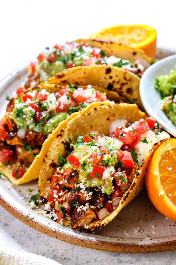 some tacos are sitting on a plate with oranges and guacamole