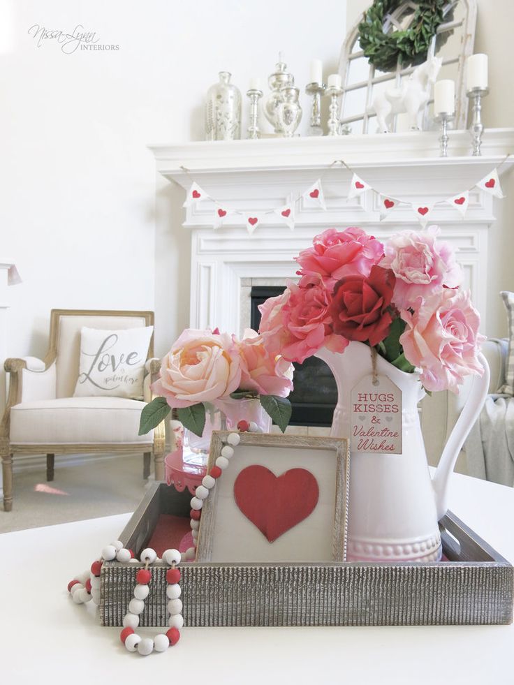 a white vase with pink flowers in it on top of a table next to a fireplace