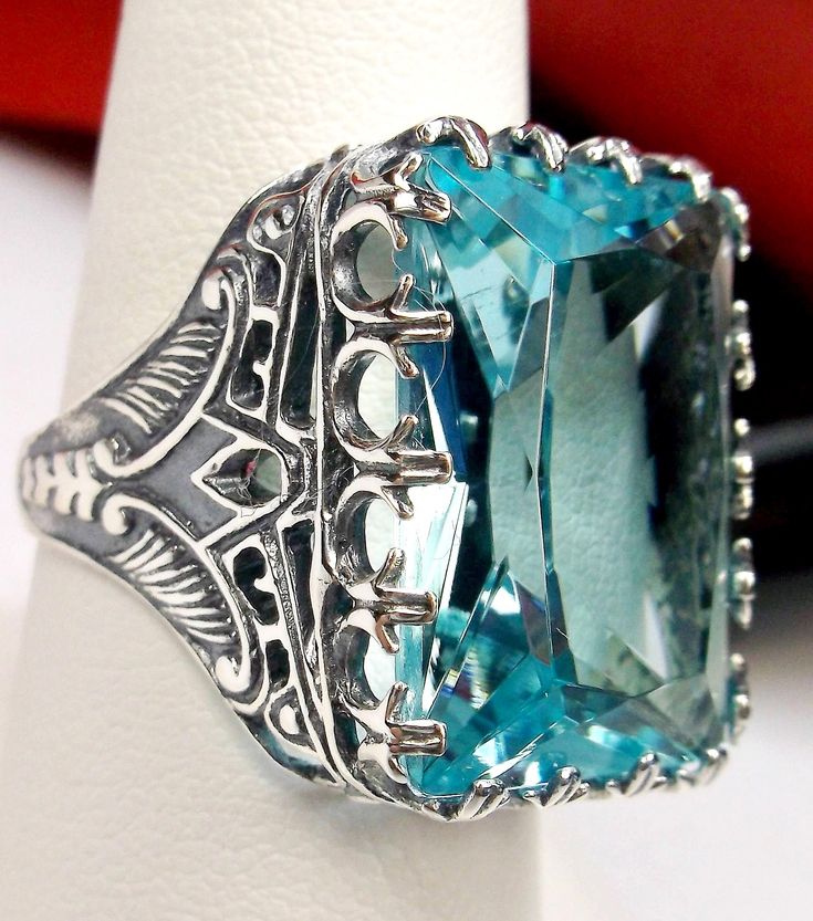 Simulated Blue Aquamarine Ring Cardinal Design#215 Custom Made I now offer this is a brand new Art Deco reproduction ring in solid sterling silver. The gorgeous filigree ring is set with a flawless huge 30ct Man-made/simulated aquamarine gemstone. The high quality rectangle cut simulated aquamarine is 20mm in length by 15mm in width (5/8th inch by 11/16th inch). the ring sits 9mm off the finger. The inside of the band is marked 925 for sterling. Notice the beautiful swirl like craftsmanship of t Cardinal Design, Art Rings, New Art Deco, Pink Topaz Ring, Blue Aquamarine Ring, Mystic Fire Topaz, Order Design, Aquamarine Ring, Pink Topaz