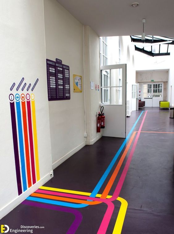 a hallway with colorful lines painted on the floor and white walls, leading to an office building