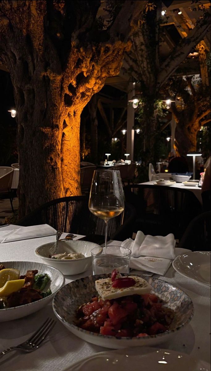 a table topped with plates of food next to a glass of wine and a tree