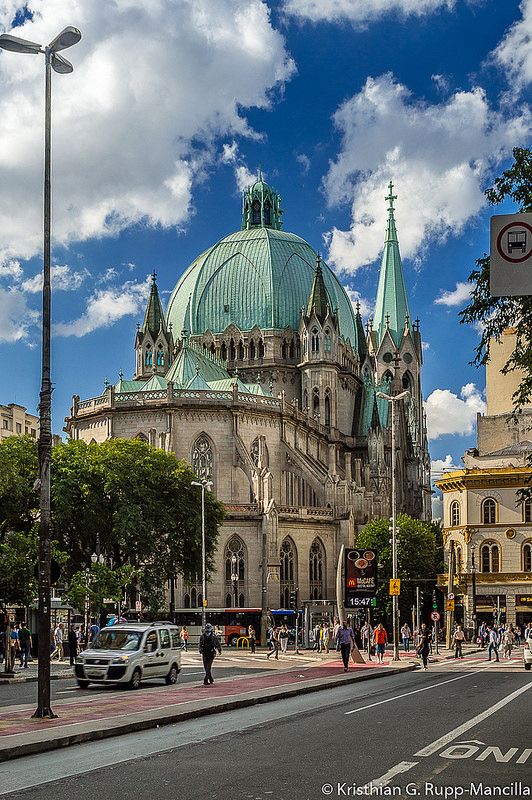 a large building with a green dome on the top and people walking around in front