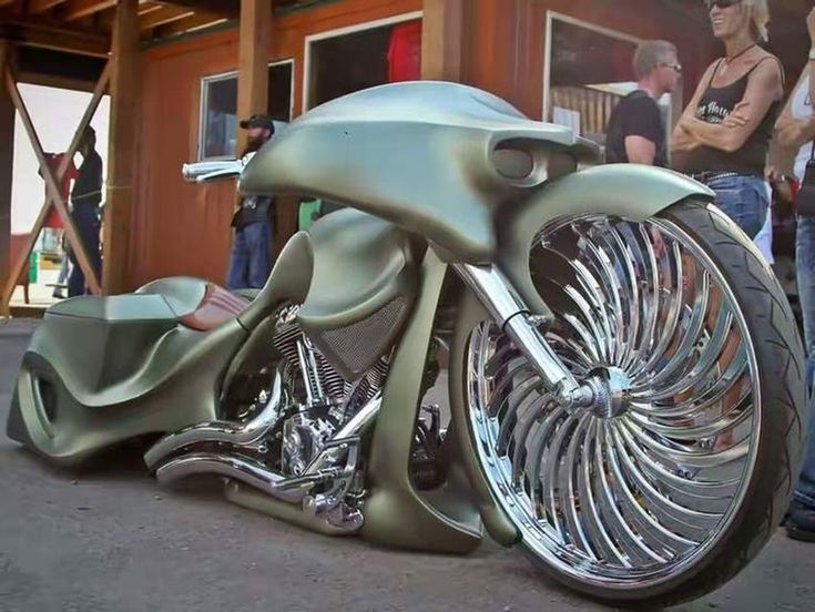 a green motorcycle parked in front of a building with people looking at the bikes on display