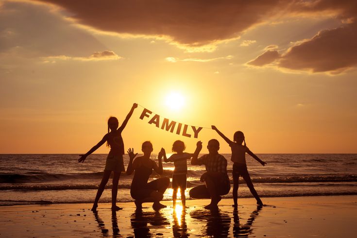 four people standing on the beach with their arms in the air and one person holding up a sign that says family