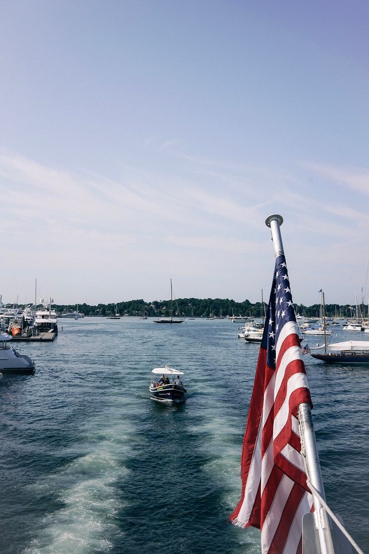 the american flag is waving in the wind as boats are on the water behind it