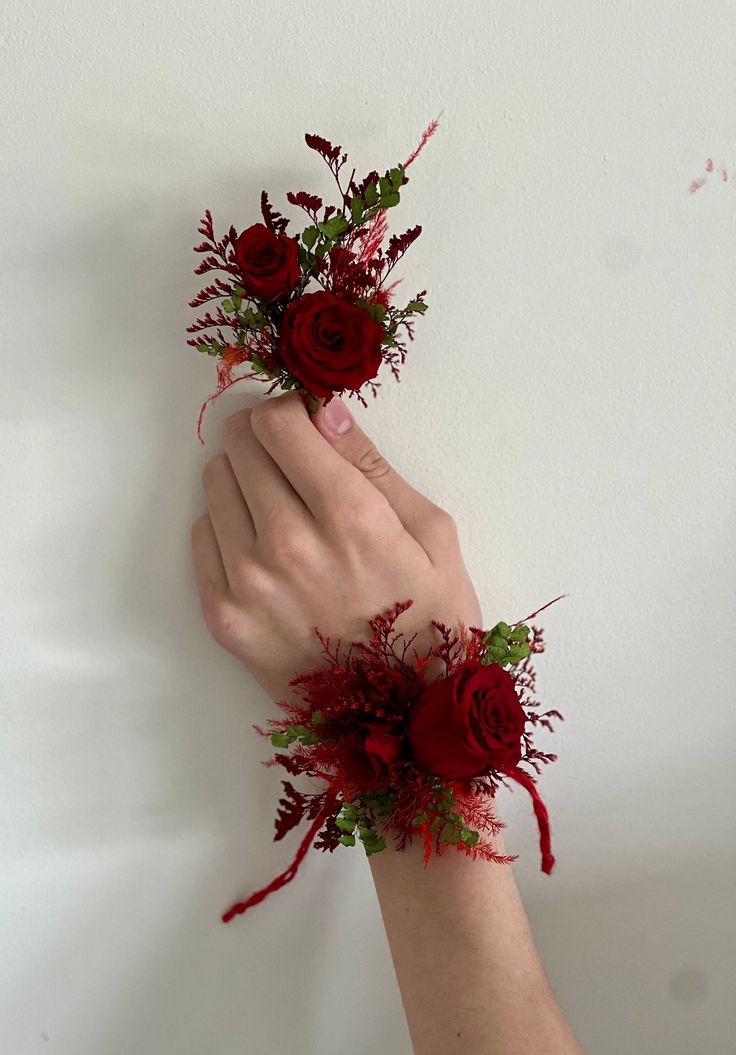 two hands holding red flowers against a white wall