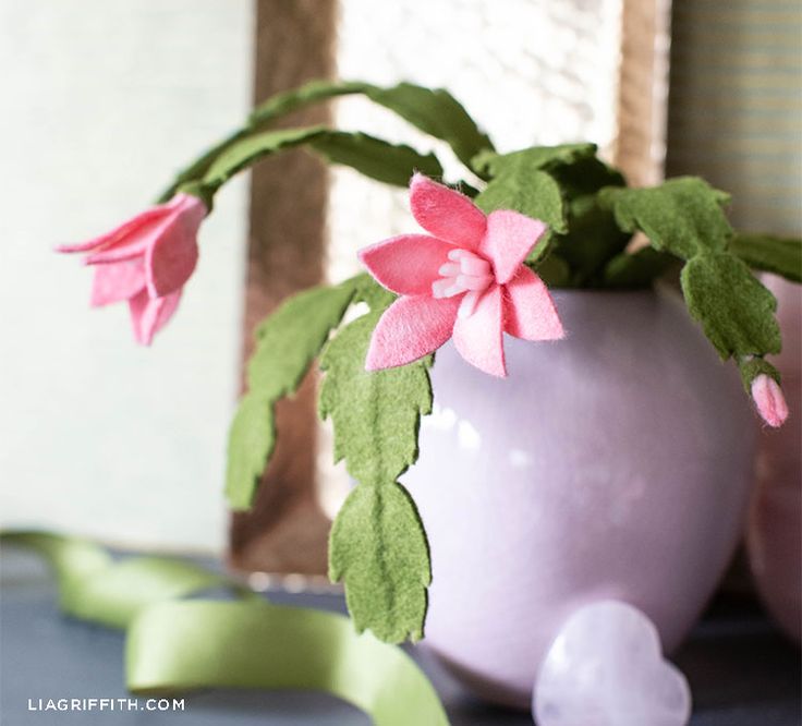 pink flowers are in a white vase with green leaves on the table next to ribbon