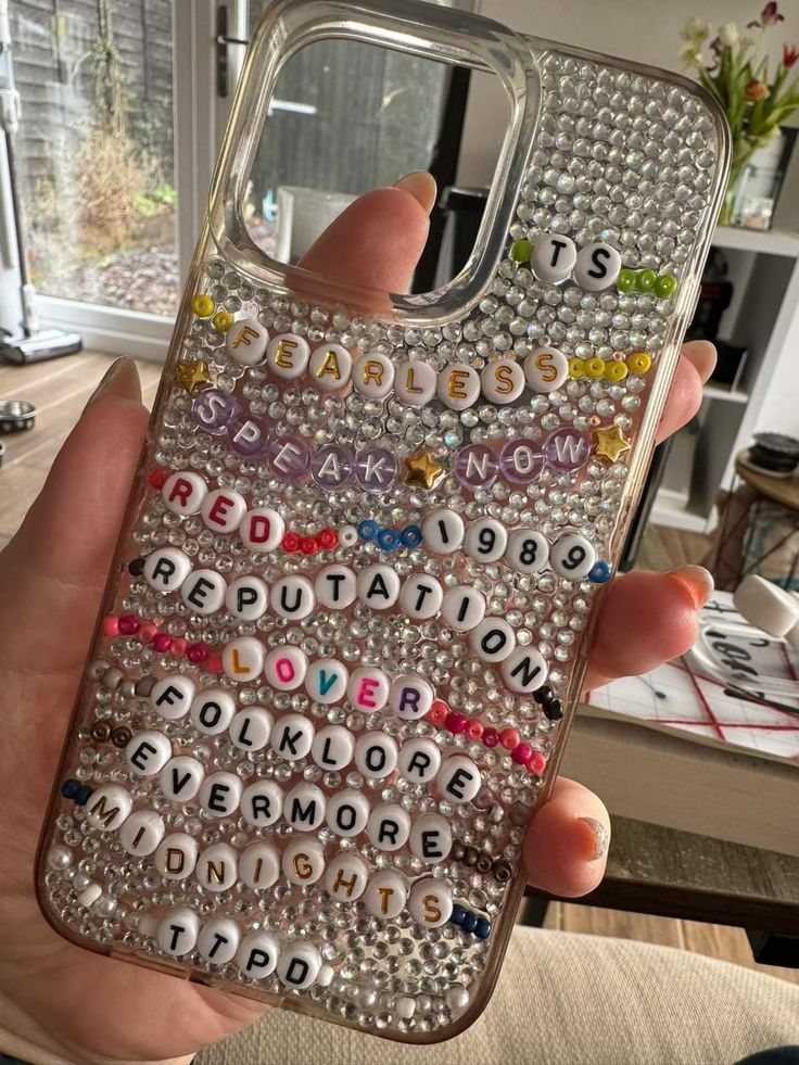 a person holding a cell phone with letters on the back and beads in the front