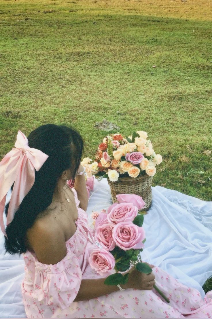 a woman sitting on top of a blanket next to a basket filled with pink roses