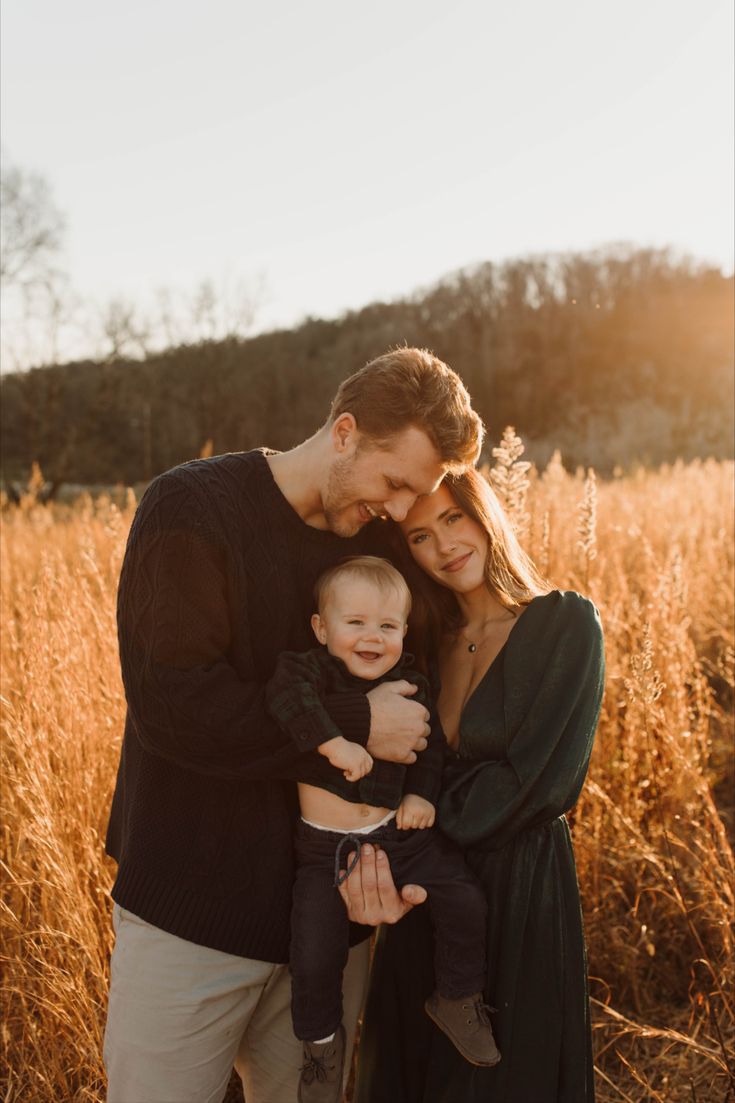 a man, woman and baby are standing in the tall grass with their arms around each other