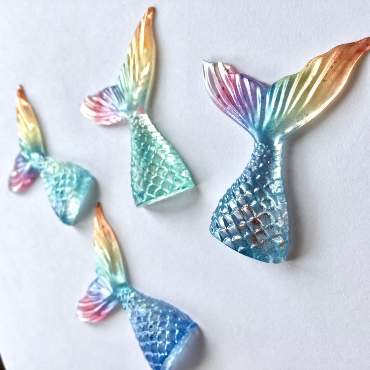 three mermaid tail shaped glass magnets sitting on top of a white table next to each other