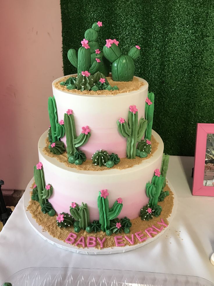 a three tiered cake decorated with pink flowers and green cactuses is on a table