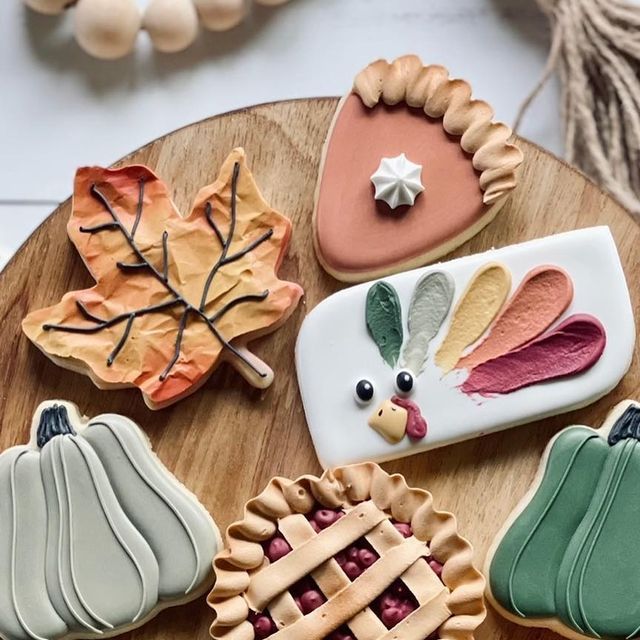 several decorated cookies sitting on top of a wooden table next to pumpkins and leaves