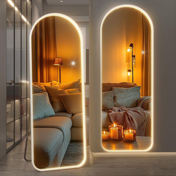 two mirrors that have lights on them in front of a couch and table with candles