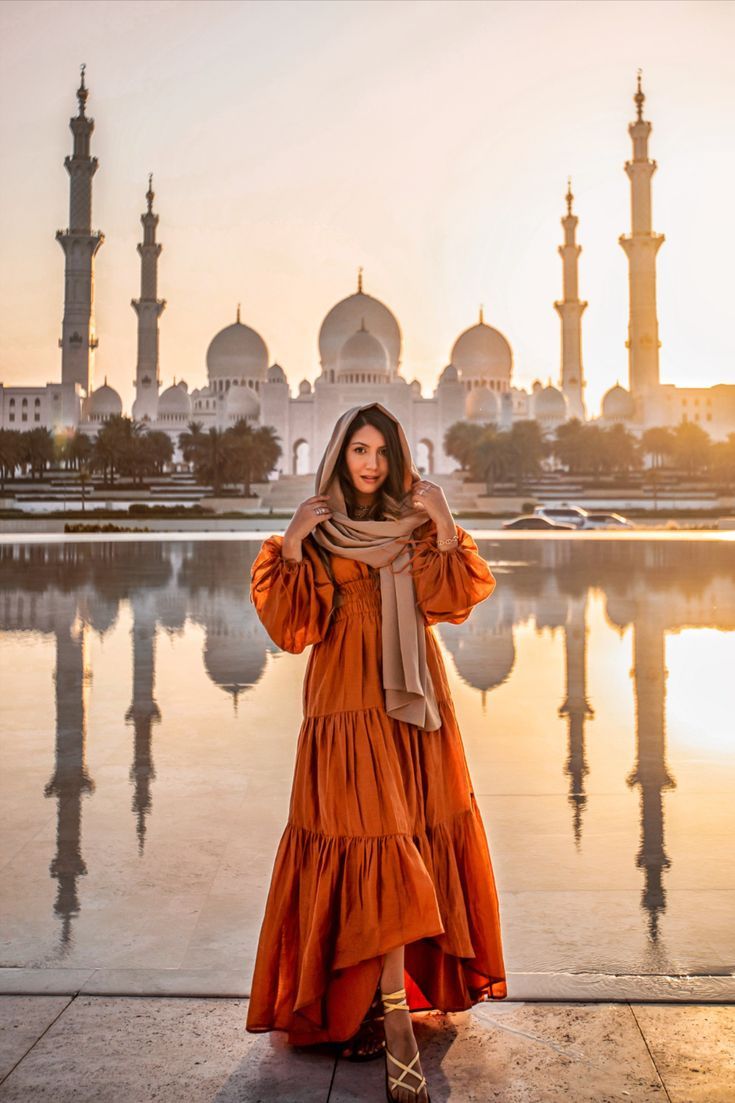 a woman standing in front of a body of water wearing an orange dress and scarf