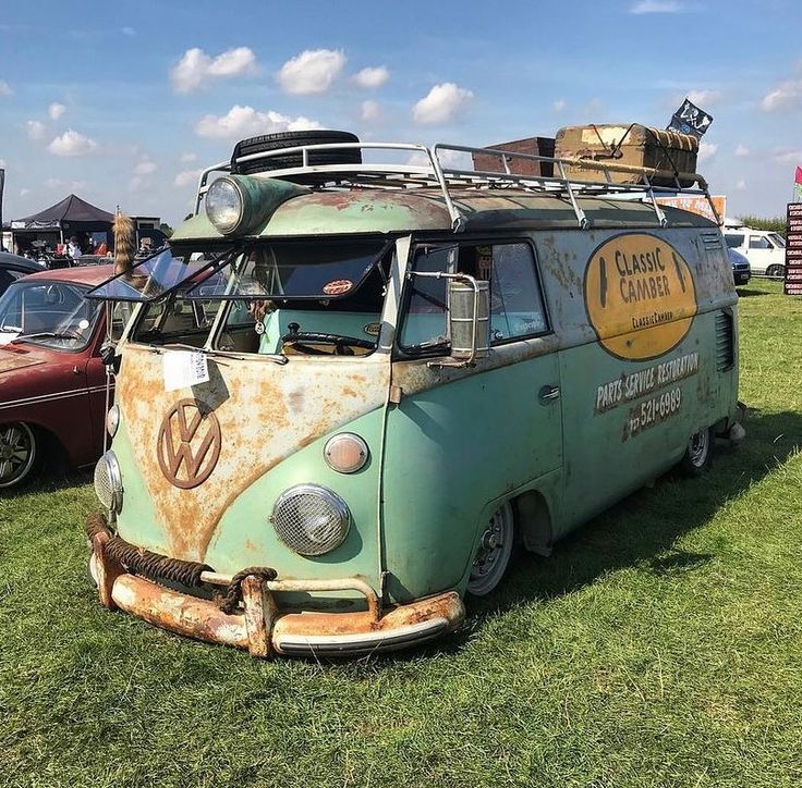 an old vw bus is parked on the grass with other cars in the background