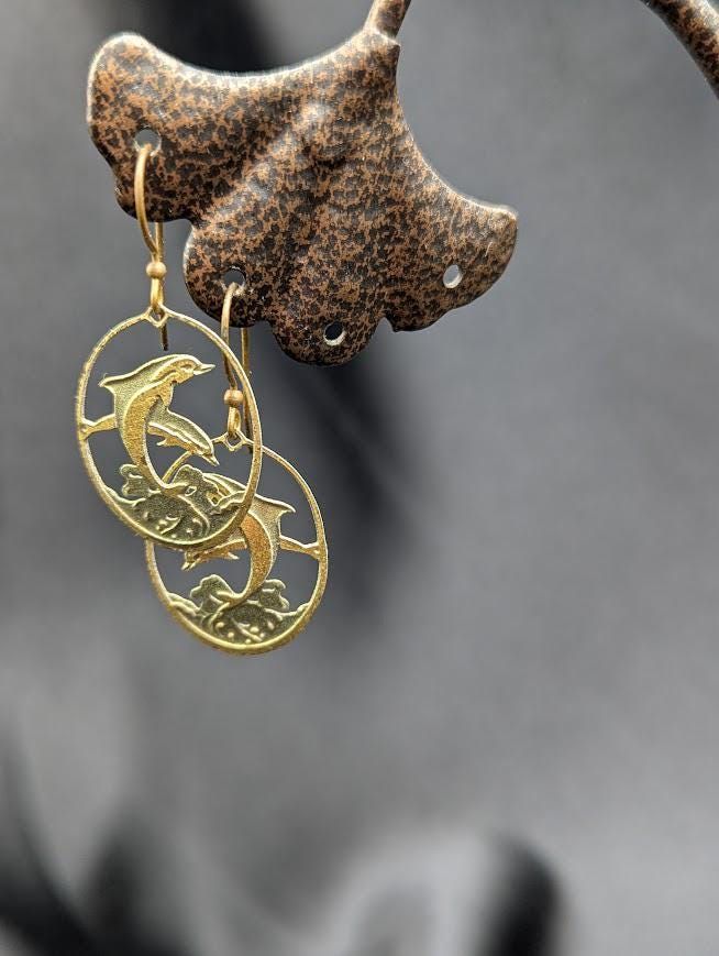 a pair of gold earrings hanging from a hook on a metal pole with a dog head in the background