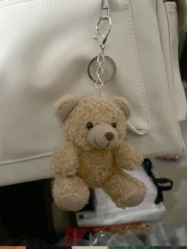 a teddy bear is hanging from a white purse with a keychain attached to it